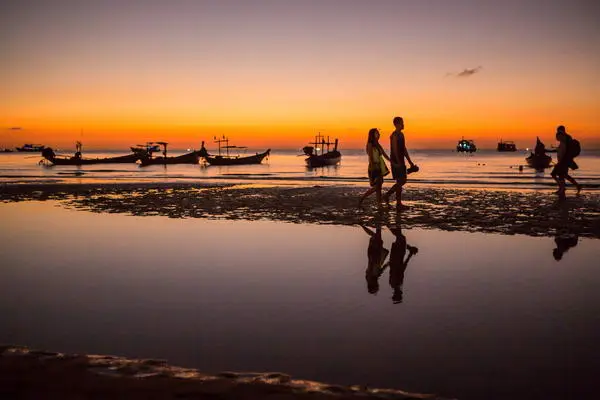 a couple walking and in hand along Sairee beach with stuning sunset behind